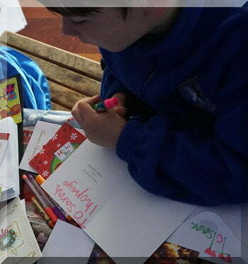 Boy writing Christmas cards - the photo shows his hand holding a pen over some childish writing