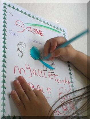 A child's hands and hair as she writes a letter to Santa (asking for My Little Pony)