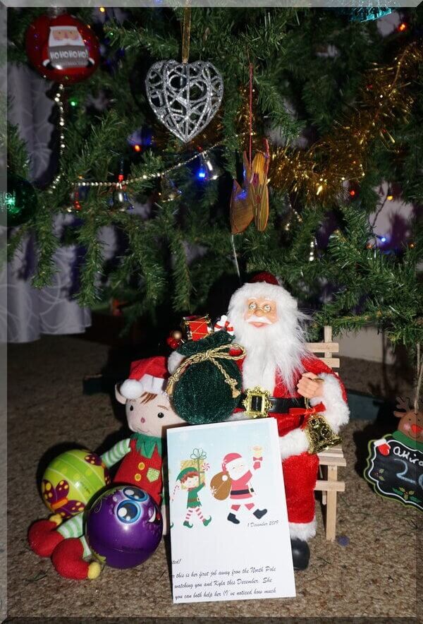 Tinkles the elf sitting by Santa under the Christmas tree