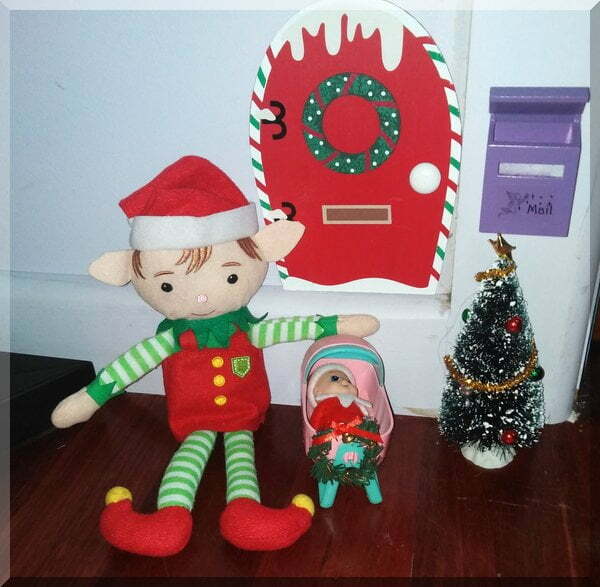 | love santa Christmas elf beside a Christmas tree and a baby elf in a pink cradle