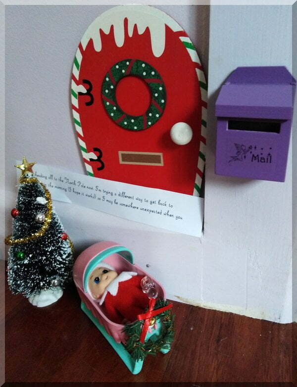 Baby elf in cradle beside a Christmas tree and letter box with a note from Tinkles the Christmas Elf