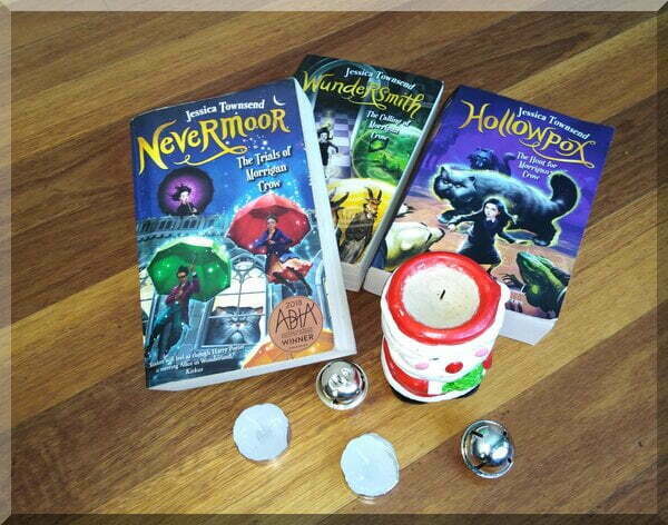 the first three books of the Nevermoor book series besides a Santa candle