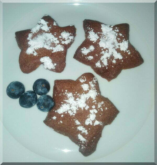 Icing sugar dusted star-shaped pepparkakor on a plate with some blueberries for a Christmas treat