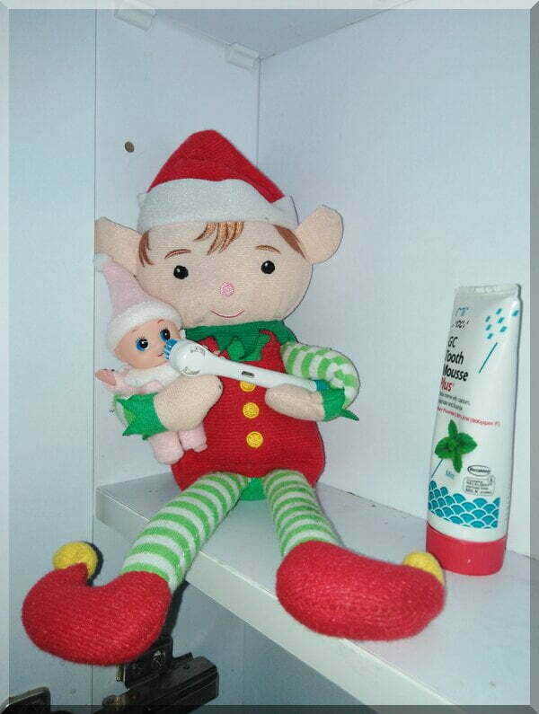 Christmas elf holding baby elf and a toothbrush to clean the baby's teeth