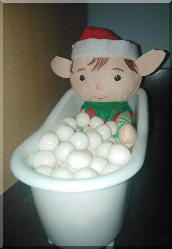 Christmas elf sitting in a bath with white balls as bubbles