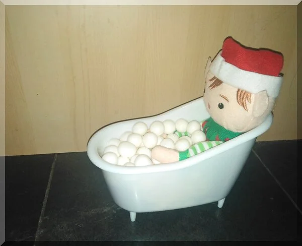 Christmas elf sitting in a bath with white balls as bubbles