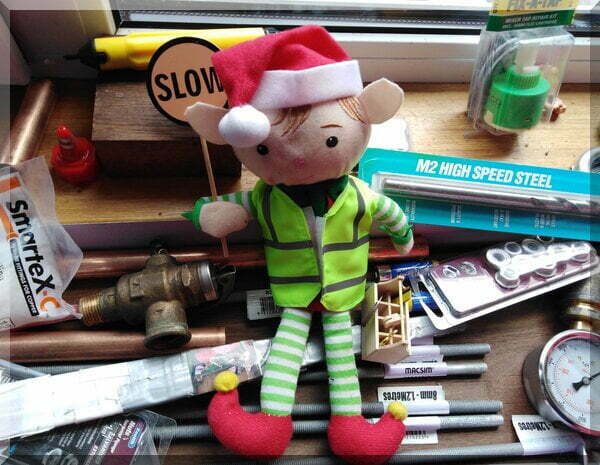 Christmas elf in a high vis vest holding a stop sign and sitting on various plumbing items