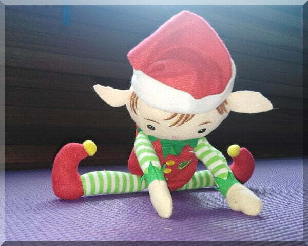 Christmas elf doing a forward bend from the splits on a yoga mat
