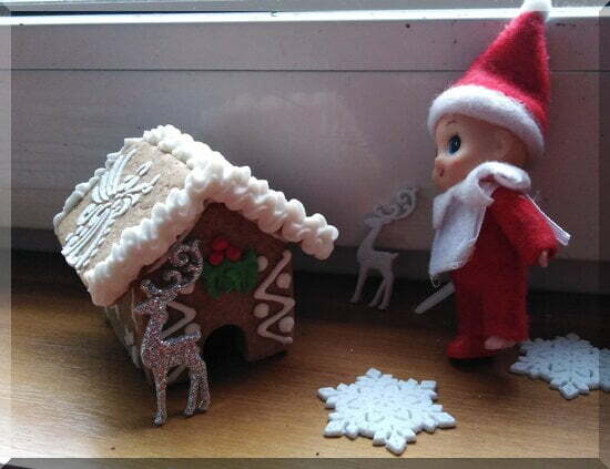 Ginger-gingerbread-house-reindeer-snowflakes_550 | love santa A baby Christmas elf in a red suit beside a gingerbread house and some glittering silver reindeer