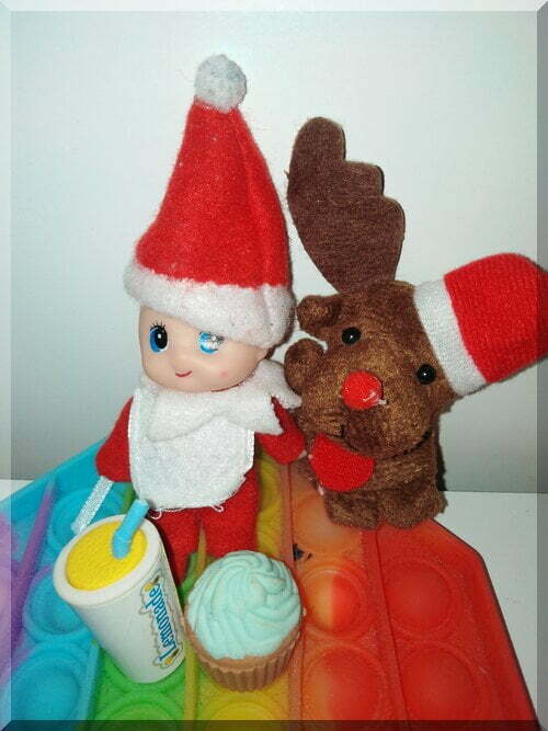 Baby Christmas elf and reindeer finger puppet sitting on a rainbow poppit with a cup of lemonade and a cupcake