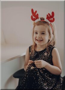 Smiling girl in a black with gold starsdress and red Christmas antlers headband