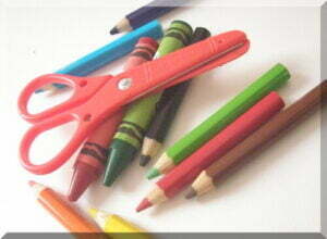 Pair of red chidlren's scissors on top of coloured pencils and crayons