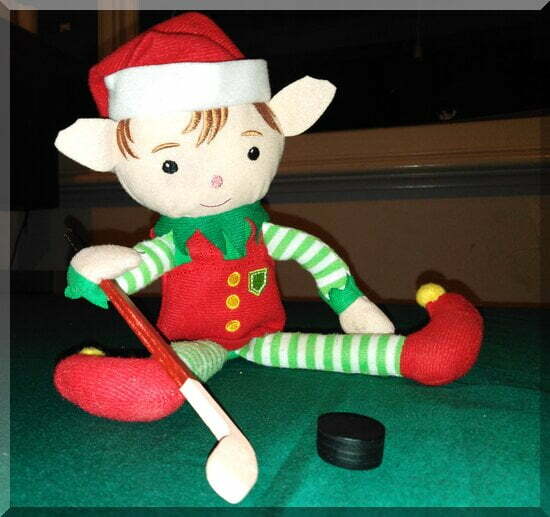 Tinkles the CHristmas elf holding a hockey stick in front of a black puck