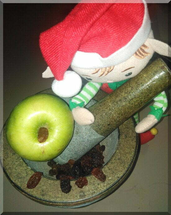 Christmas elf holding a pestle to mince an apple and some sultanas in a stone mortar