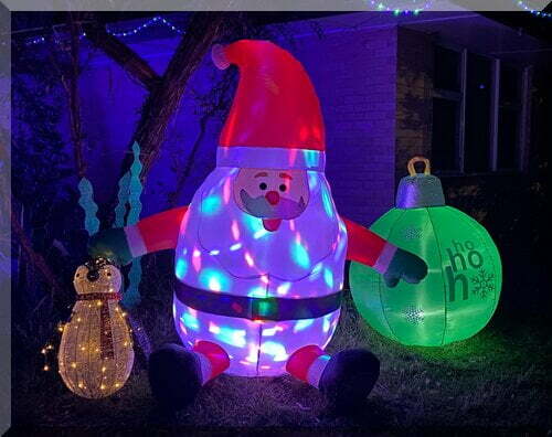 A white penguin with lights beside an inflatable round Santa and a large green bauble
