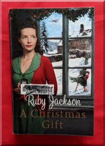 Front cover of "A Christmas Gift" showing a young woman dressed in 1940s clothes in front of a window with a snowy village outside