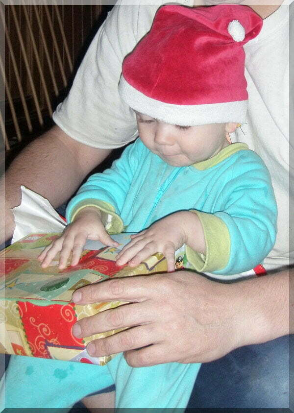 Photo of a baby boy in a Santa hat opening a Christmas present