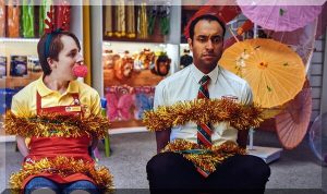 Two men looking sad as they are tied up with tinsel and Christmas lights in a toy store